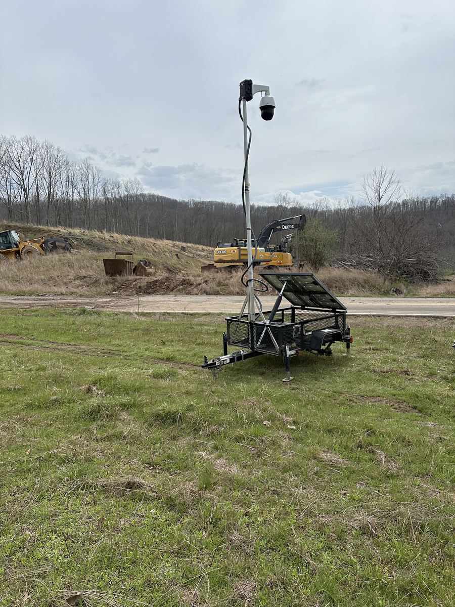 Solar surveillance trailer with PTZ camera beside an excavator
